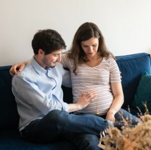 Femme enceinte et son conjoint sur leur canapé lors d'une séance grossesse paris, photographe de grossesse
